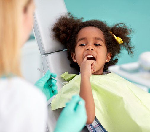 Young girl in dental chair pointing to her tooth